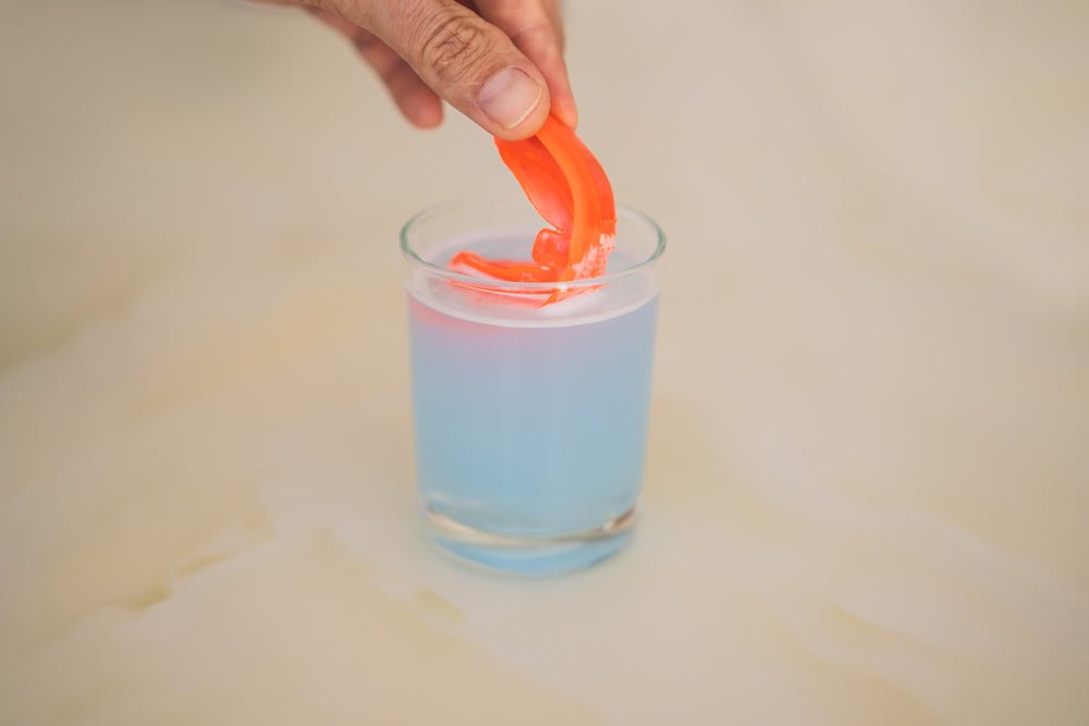 Hand dipping orange mouthguard in cleaning solution